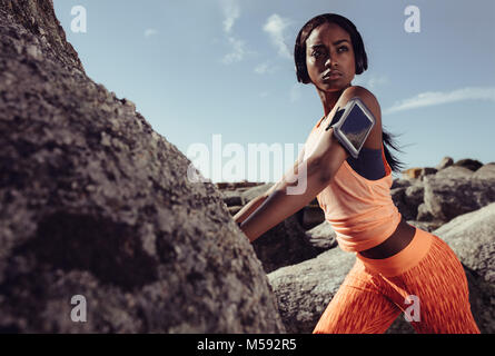Fit donna africana in piedi sulla roccia in spiaggia durante la sessione di allenamento. donna fitness in abbigliamento sportivo durante una sessione di allenamento all'aperto. Foto Stock