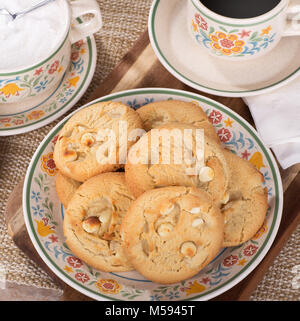 Pila di noce macadamia cookie su una piastra con la tazza di caffè e zuccheriera Foto Stock