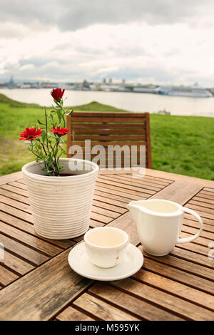 Bianco vuoto tazza di caffè e un fiore bianco vaso con margherite rosso outdoor in Videy isola vicino a Reykjavik, Islanda. Foto Stock