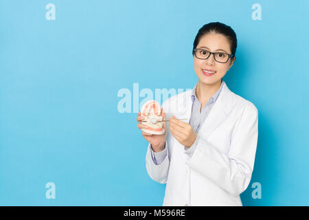 Fiducioso piuttosto ospedale medico donna con specchio dentale attrezzo ispezione dello stampo di dente che mostra la cura orale concetto isolato su sfondo blu. Foto Stock