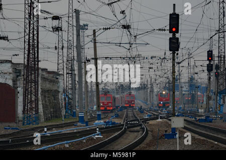 Tre tipici treni russi nel mezzo di una massa di fili e portali sulle reti ferroviarie siberiano Foto Stock