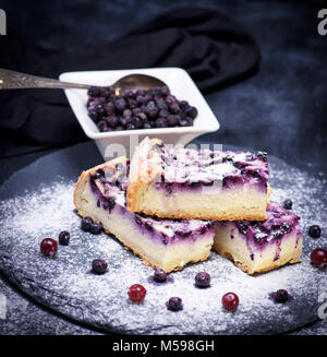 Pezzi di torta di ricotta e mirtilli su uno sfondo nero spolverati con zucchero a velo Foto Stock