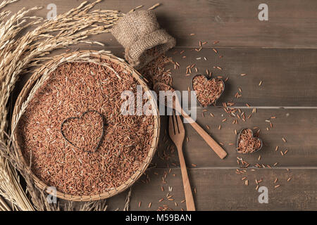 Marrone tailandese di riso al gelsomino o riso berry nel cestello di bambù e su uno sfondo di legno, amore riso biologico e cibo sano Foto Stock