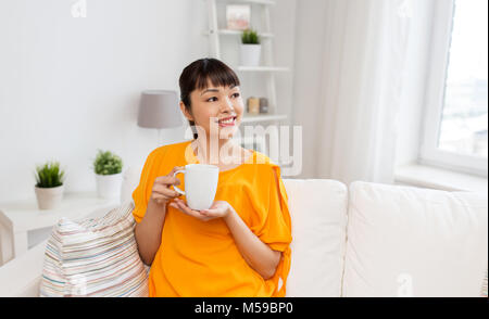 Felice donna asiatica bere il tè o il caffè a casa Foto Stock