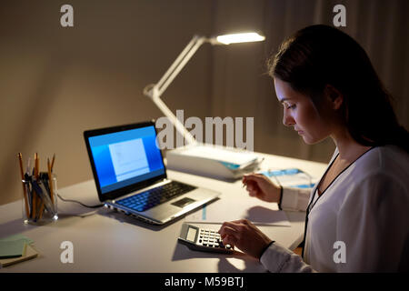 Donna con la calcolatrice e carte di notte office Foto Stock