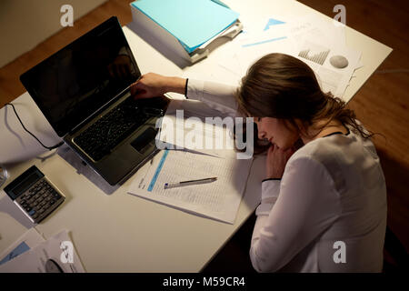 Stanco della donna che dorme sul tavolo per ufficio di notte Foto Stock