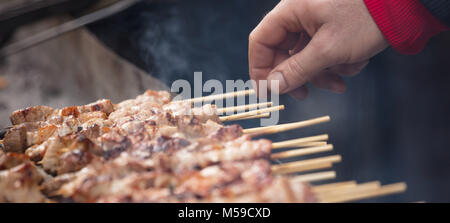 Gli spiedini di carne souvlaki sul barbecue. Mano d'uomo gira sull'altro lato gli spiedini sulla griglia. Close up, vista frontale, banner. Foto Stock