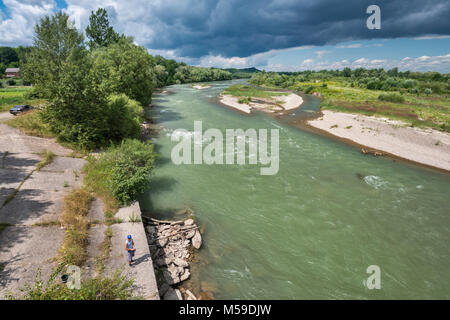 L'uomo la pesca nel fiume Prut sotto le nuvole scure visto dal ponte dell'autostrada vicino Luzhany, Bukovina regione, Oblast di Chernivtsi, Ucraina Foto Stock