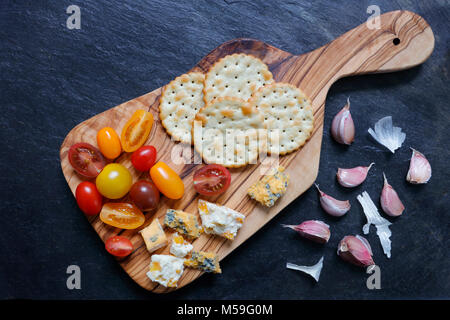 Un assortimento di coloratissimi pomodorini con olive e aglio su ardesia con cracker Foto Stock