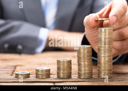 Sezione mediana di imprenditore di monete di impilamento in ordine crescente sul tavolo di legno Foto Stock