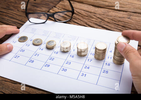 Mani tagliate di imprenditore di monete di impilamento in ordine crescente sul calendario Foto Stock