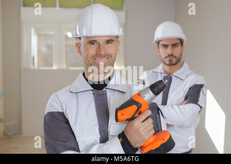 Gruppo di costruttori sorridente in hardhats con trapano elettrico per interni Foto Stock