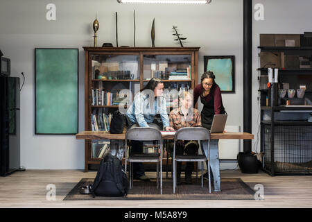 Tre donne riuniti intorno al tavolo in zona ufficio di un metallo in officina. Foto Stock