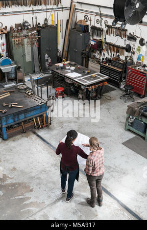 Angolo di alta vista di due donne in piedi in metallo, officina azienda blueprint tecnici. Foto Stock