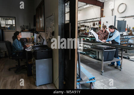 Due donne a una scrivania in ufficio area di un workshop di metallo, donna in piedi al banco di lavoro mobile. Foto Stock