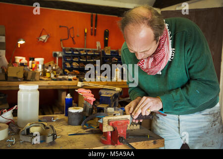 Un coltello maker in un workshop mettendo con cautela la lama di un coltello da cucina in una morsa sul banco di lavoro. Foto Stock