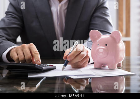 I mediatori il calcolo di Bill con il Rosa Piggybank sulla scrivania Foto Stock