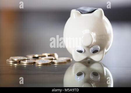 Close-up di Piggybank Capovolto vicino a monete metalliche sulla scrivania Foto Stock