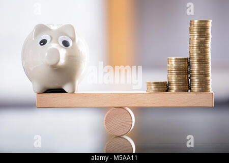 Close-up di Piggybank e monete impilate in equilibrio su altalena in legno Foto Stock