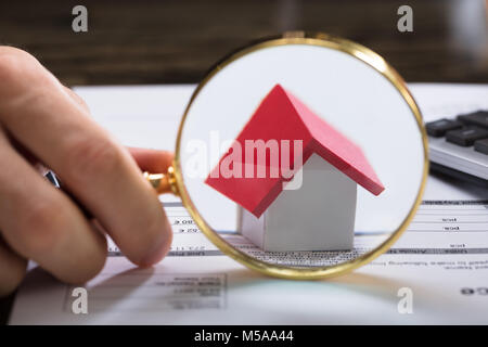 Close-up di un imprenditore la mano con lente di ingrandimento zoom sul modello di casa Foto Stock