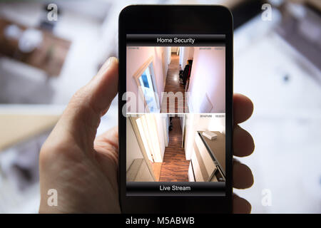 Close-up di mano di una persona servendosi di un sistema di sicurezza domestica sul telefono cellulare Foto Stock