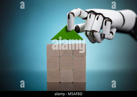 Il Robot la mano della casa di costruzione del blocco di legno su sfondo grigio Foto Stock