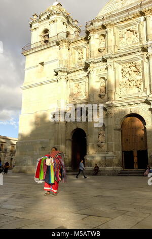 Il sole tramonta maestosamente su una donna in piedi sopportano stoicamente davanti al Cathedrral di Nostra Signora dell'Assunzione a Oaxaca, Messico. Foto Stock