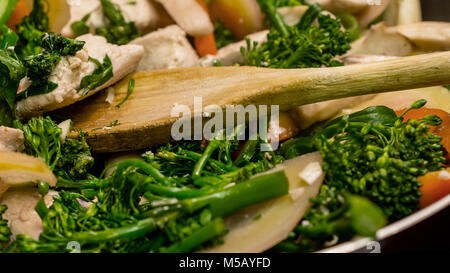Vista ingrandita del cucchiaio di legno in agitazione il pollo e le verdure in padella in ghisa - mescolare la frittura nel mondo reale Foto Stock