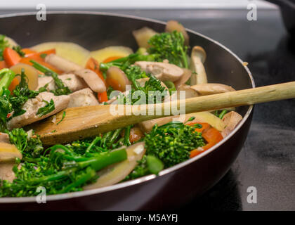 Close-up e vista laterale del cucchiaio di legno in agitazione il pollo e le verdure in padella in ghisa - mescolare la frittura Foto Stock