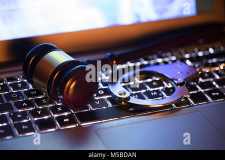 Close-up di un martello e manette sulla tastiera del notebook Foto Stock