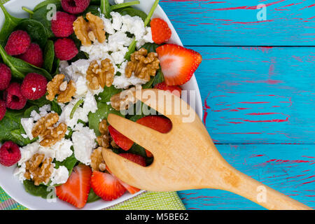 Una sana insalata con frutti di bosco freschi e formaggio feta condito con noci su un letto di baby spinaci foglie con una insalata di legno server tramite un crepitio blu pa Foto Stock