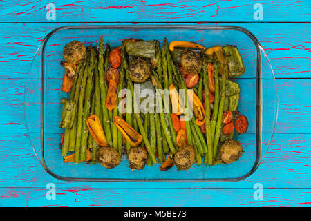 Antipasto sano di carni arrosto misto di verdure in un vetro piatto da forno con asparagi verdi, mini peperone, pomodoro e patate su un esotico blu c Foto Stock