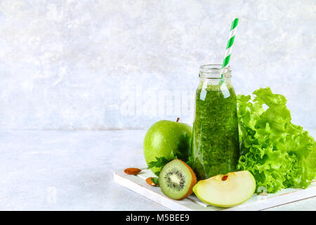 Frullati verde da prezzemolo, insalata, kiwi, Apple in una bottiglia su un calcestruzzo di colore grigio nella tabella Foto Stock
