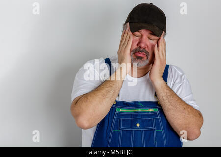 Lavoratore in tuta con un grande mal di testa tenendo la testa tra le mani con i suoi occhi chiusi contro la dolorosa frementi isolato su bianco Foto Stock