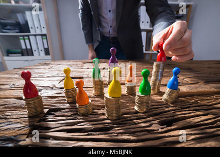 Close-up di un imprenditore la mano immissione rosso figurina pedina sulla sommità di una pila di monete d'Oro Foto Stock