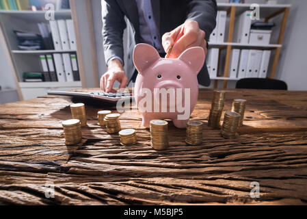 Commercianti calcolo impilati monete d oro con Rosa Piggybank sulla scrivania in legno Foto Stock