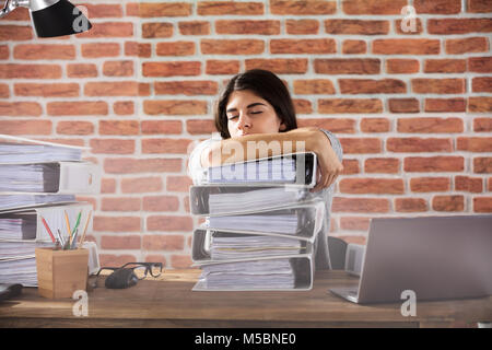 Giovane imprenditrice di dormire sulla cartella impilati sulla scrivania in ufficio al lavoro Foto Stock