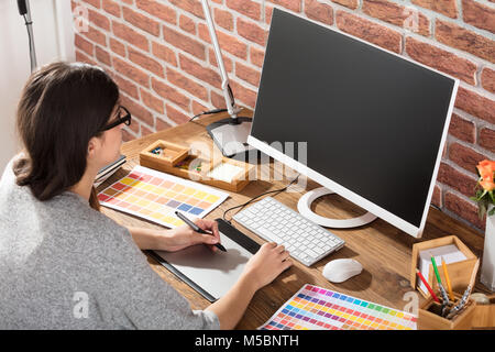 Giovani femmine Graphic Designer con tavoletta grafica con i campioni di colori sulla scrivania Foto Stock