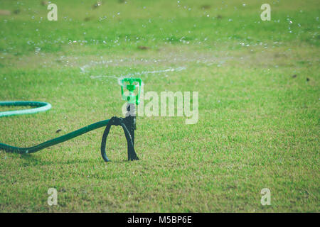 Lawn sprinkler acqua su erba verde la spruzzatura e irrigazione prato in giardino nella stagione estiva. Foto Stock