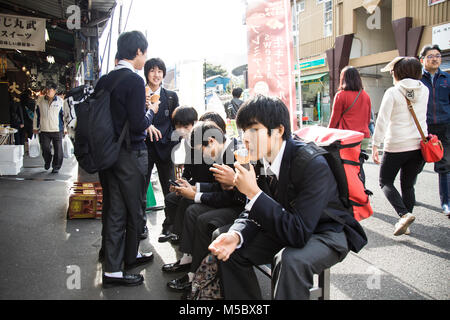 Scuola Giapponese boys gustare gelato presso il Mercato del Pesce di Tsukiji a Tokyo Foto Stock