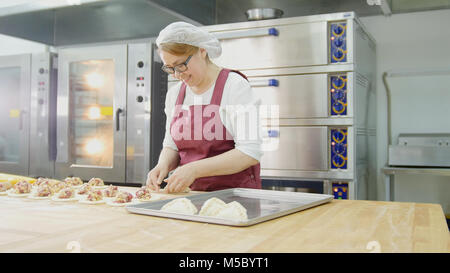 Donna adulta in occhiali e grembiule cuoce dolci al forno Foto Stock