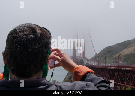 Primo piano sulla spalla vista turistica prendendo moody fotografia di Golden Gate Bridge coperti dalla nebbia. Foto Stock
