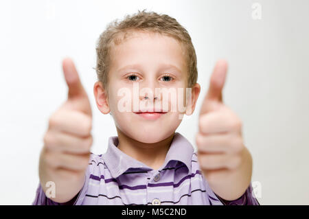 Il corpo superiore vista di un anno sette vecchio ragazzo davanti a uno sfondo bianco che mostra due pollici in su. Foto Stock