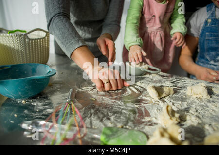 La mamma insegna due piccole figlie a cuocere dall'impasto. I bambini con piacere sono impegnati nel lavoro di cucina. Foto Stock