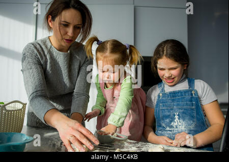 La mamma insegna due piccole figlie a cuocere dall'impasto. I bambini con piacere sono impegnati nel lavoro di cucina. Foto Stock