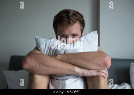 Uomo malato seduto sul suo letto con la sua testa sulla sua mano Foto Stock