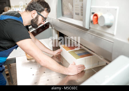 Uomo al lavoro con la macchina di taglio presso l'impianto di stampa Foto Stock