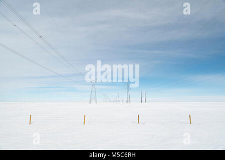 Alberta, Canada. Guardando verso il basso centro di a doppia fila di piloni di elettricità/torri di trasmissione sulle praterie d'inverno. Foto Stock