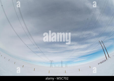 Alberta, Canada. Guardando verso il basso centro di a doppia fila di piloni di elettricità/torri di trasmissione sulle praterie in inverno, fisheye prospettiva. Foto Stock