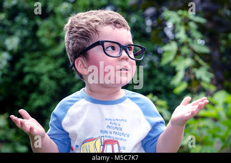 Un curioso little boy in grandi bicchieri chiede un sacco di domande, il numero uno in questione è di solito perché? Foto Stock